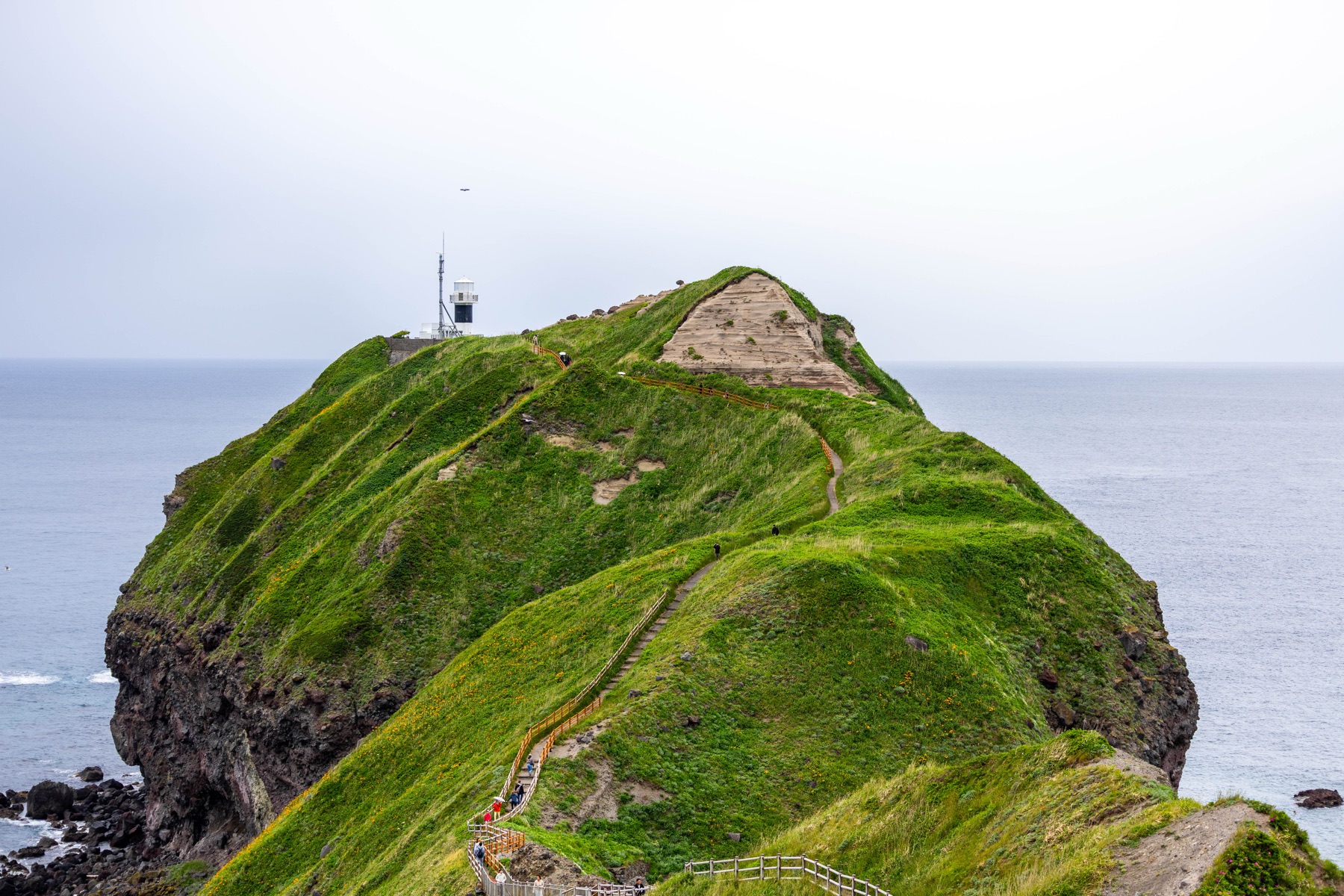 A green coastal hill with a footpath and lighthouse.